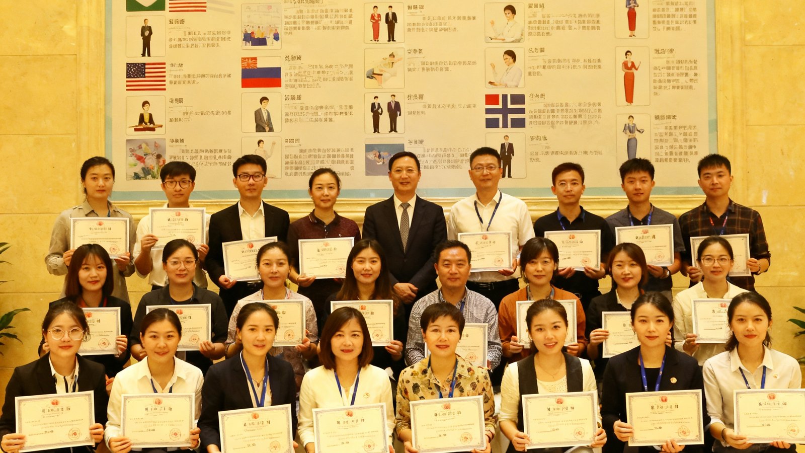 培训结业典礼上，三十余位学员手持证书与讲师合影，背景是集团培训中心的文化墙，上面展示着各国礼仪规范图示